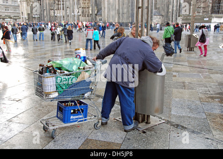 Uomo con un carrello della spesa il deposito di raccolta bottiglie da un cestino dell'immondizia in piazza duomo a fianco di inizio Foto Stock