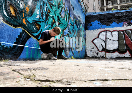 Dieci-anno-vecchio ragazzo giocando con il suo Nintendo di fronte a un muro di graffiti Foto Stock