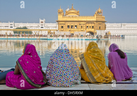 Le donne indiane, pellegrini indossa sari colorati seduta sul bordo del bacino idrico di l'Amrit Sagar, o lago Santo, Harmandir Foto Stock
