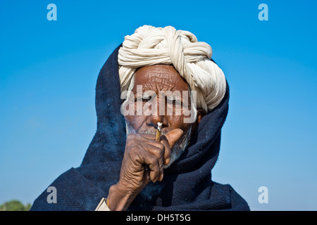 Uomo indiano con un turbante bianco fumare una sigaretta bidi, Pushkar, Rajasthan, India Foto Stock