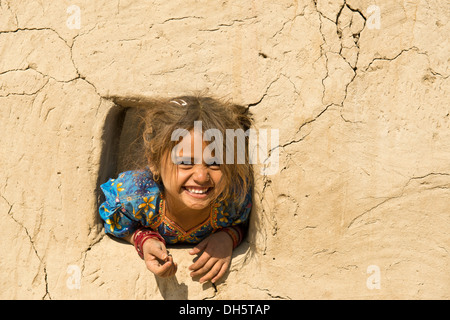 Bambina si appoggia al di fuori di un'apertura di una finestra in una casa di fango, Gujarat, India Foto Stock