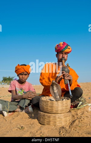 Rajasthani incantatore di serpente con un turbante, riproduzione di un flauto, un cobra o Naja avvolgimento da un cestello davanti a lui Foto Stock