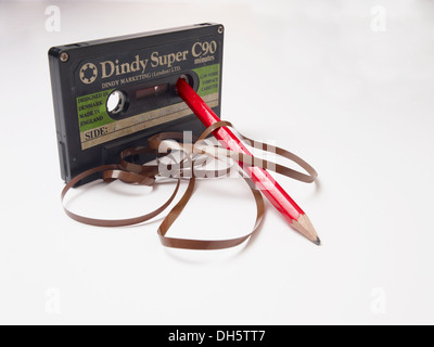 Super Dindy Audio cassetta con il nastro che fuoriesce su un tavolo bianco formando motivi curly sudicio con una matita per avvolgere il nastro con Foto Stock