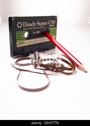 Super Dindy Audio cassetta con il nastro che fuoriesce su un tavolo bianco formando motivi curly sudicio con una matita per avvolgere il nastro con Foto Stock