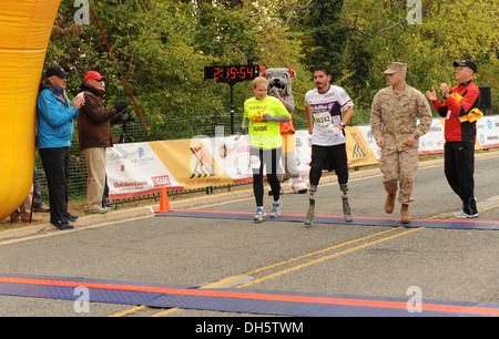 Un partecipante attraversa la linea del traguardo della trentottesima annuale di Marine Corps Marathon come sostenitori e volontari evento allietare lui a. Foto Stock