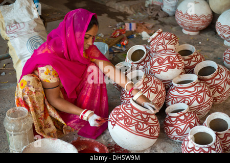 Donna indiana indossando un velo seduto sul pavimento e dipinto di argilla vasi di acqua con tradizionali decorazioni, Jodhpur Foto Stock