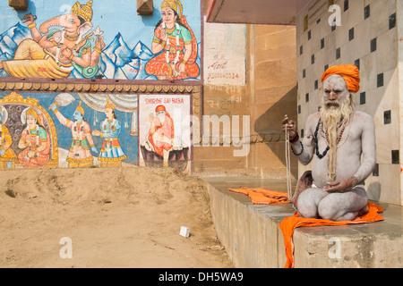 Sadhu, un santo uomo o errante seduta ascetica meditando su un asciugamano, il suo corpo è cosparso di cenere bianca nel segno di Shiva, Foto Stock