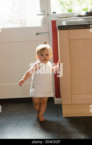 Nove mesi di apprendimento ragazza di alzarsi e camminare sul pavimento della cucina. Inghilterra, Regno Unito. Foto Stock