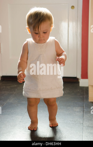 Nove mesi di apprendimento ragazza di alzarsi e camminare sul pavimento della cucina. Inghilterra, Regno Unito. Foto Stock