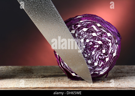 Primo piano di una testa di cavolo rosso e un intaglio coltello. Formato orizzontale su un rustico di superficie di legno e un caldo dello sfondo. Foto Stock