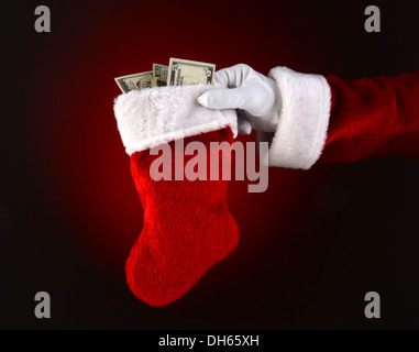 Primo piano di Santa Claus tenendo una calza piena di contanti. Solo Santa la mano e il braccio su una luce di colore rosso scuro dello sfondo. Foto Stock