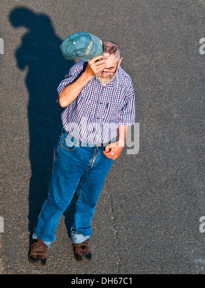 Tettuccio di vista posteriore di uomo anziano camminando per strada / sollevamento hat / graffiare la testa - Francia. Foto Stock