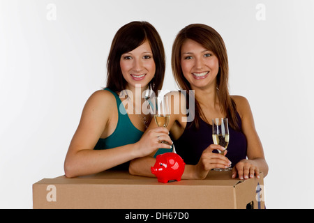 Due giovani donne di casa in movimento con un salvadanaio e bicchieri di champagne Foto Stock