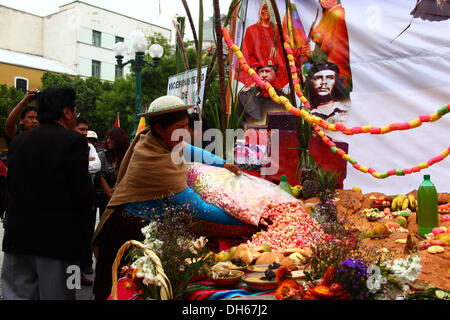 LA PAZ, BOLIVIA, 1 novembre 2013. Una signora riversa pasankalla (boliviano dolce fatto di mais tostato, un po' come popcorn) su un tipico altare (o mesa) che sono costruiti per ricevere le anime dei suoi cari per Todos Santos. La cerimonia è stata organizzata dal Ministero della decolonizzazione in onore delle popolazioni indigene e l'ala sinistra eroi, comprese Che Guevara e Hugo Chavez (entrambi raffigurata sul poster). Credito: James Brunker / Alamy Live News Foto Stock