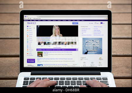 Il sito web di Yahoo su un MacBook contro una panca in legno sfondo all'aperto tra cui un uomo le dita (solo uso editoriale). Foto Stock
