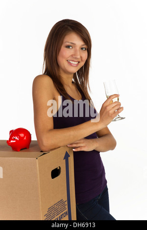 Giovane donna con una scatola di movimentazione e un bicchiere di champagne in mano, sorridente Foto Stock