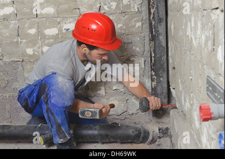 Un elettricista e meccanico dei sistemi di ingegneria sanitaria, riscaldamento e aria condizionata, installando un tubo fognario Foto Stock