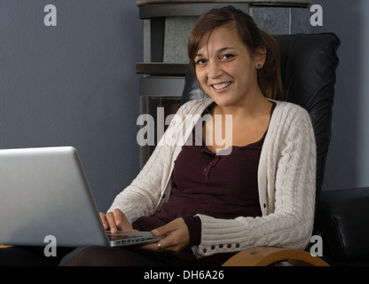 Una giovane donna di origine indonesiana è seduto di fronte ad un bruciatore di legno lavorando su un computer portatile Foto Stock