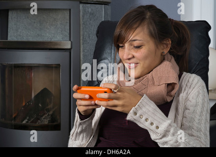 Una giovane donna di origine indonesiana è seduto di fronte ad un bruciatore di legno lavorando su uno smartphone Foto Stock