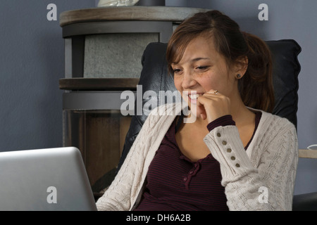 Una giovane donna di origine indonesiana è seduto di fronte ad un bruciatore di legno lavorando su un computer portatile Foto Stock