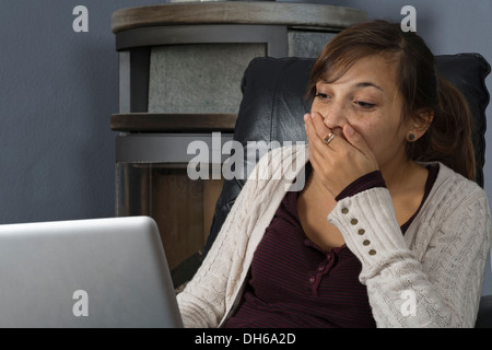 Una giovane donna di origine indonesiana è seduto di fronte ad un bruciatore di legno lavorando su un computer portatile Foto Stock