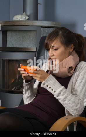 Una giovane donna di origine indonesiana è seduto di fronte ad un bruciatore di legno lavorando su uno smartphone Foto Stock