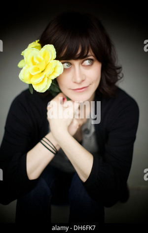 Adorabili attrice tazze per la fotocamera mentre si indossa un gigante giallo fiore nei suoi capelli. Foto Stock