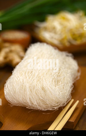 Il riso grezzo noodles su tavola di legno con bacchette sul lato e verdure in retro Foto Stock