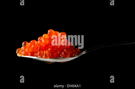 Caviale rosso in cucchiaio di metallo isolato su sfondo nero Foto Stock