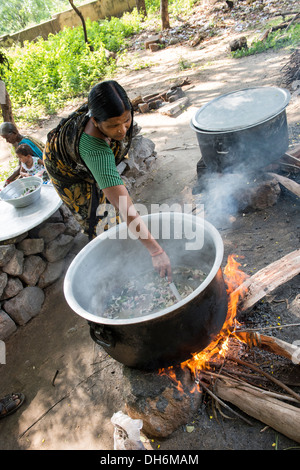 Donna indiana cucinare i pasti scolastici su fuochi aperti in corrispondenza di una zona rurale villaggio indiano di alta scuola. Andhra Pradesh, India Foto Stock