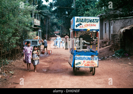 Ice Cream vendor spingendo il suo vecchio carrello giù un fango rurale via strada di Goa in India Foto Stock