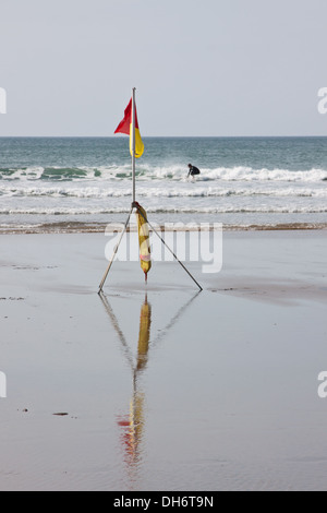 Un surfista cavalca l'onda sulla costa della Cornovaglia REGNO UNITO fuori una spiaggia sorvegliata da bagnini dal Royal National Lifeguard per istituzione Foto Stock