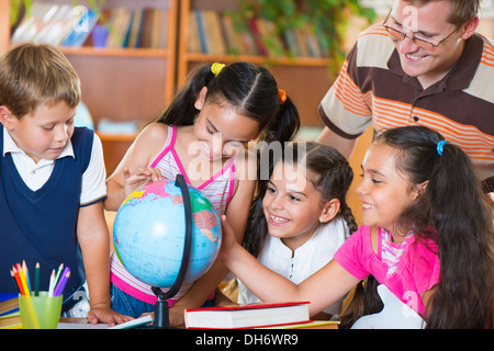 Ritratto di alunni guardando il mondo con il loro insegnante durante la lezione di geografia Foto Stock