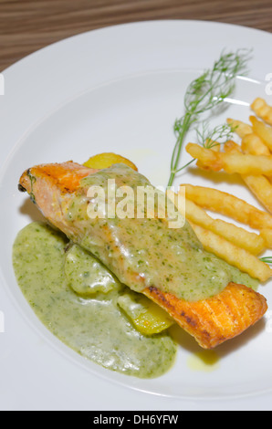 Salmone arrosto servita con salsa verde e patatine fritte sulla piastra bianca Foto Stock