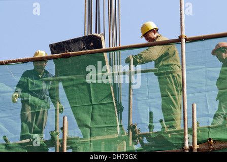 Costruttori che utilizzano una gru per caricare il cemento in un cantiere a Pechino, mentre lavorano alla costruzione di un nuovo edificio sostenuto da ponteggi. © Olli Geibel Foto Stock