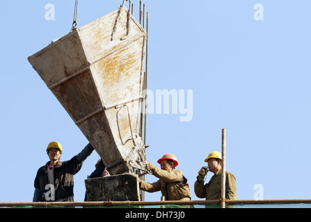 Costruttori che utilizzano una gru per caricare il cemento in un cantiere a Pechino, mentre lavorano alla costruzione di un nuovo edificio sostenuto da ponteggi. © Olli Geibel Foto Stock