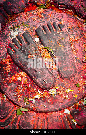 Dipinto di rosso Buddha due piedi di fiori di riso e monete offerte vicino santuario buddista Swayambhunath Stupa Monkey Temple Nepal Foto Stock