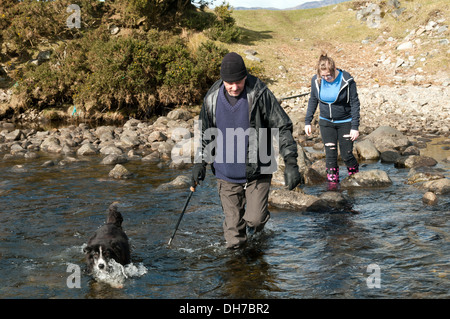 Due escursionisti e un cane guadare il Abhainn Inbhir Guiserein river a Inverguseran, Knoydart, regione delle Highlands, Scotland, Regno Unito Foto Stock