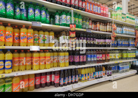 Una varietà di bottiglie di frizzanti bevande zuccherate per la vendita in un supermercato Tesco ripiani del corridoio. Regno Unito, Gran Bretagna Foto Stock