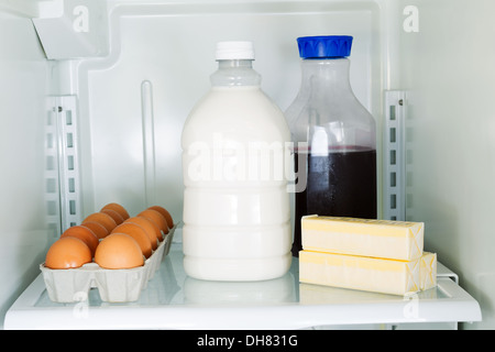 Foto orizzontale di latte, uova, burro e succo di frutta sulla mensola in vetro interno del frigorifero Foto Stock