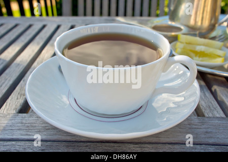 Tazza di tè nero servita su un tavolo di legno in un giardino. Foto Stock