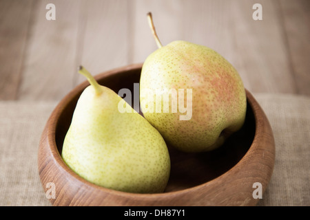 Due pere con macchiettato di verde pallido pelle tinte di rosa in una ciotola di legno con un panno di lino su una superficie in legno Foto Stock