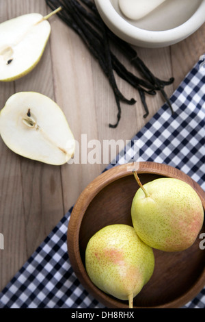 Il pestello e mortaio, tutto il Madagascan baccelli di vaniglia e le pere su una superficie in legno con ciotola di legno e blu panno controllati Foto Stock