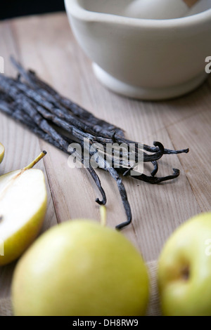 Il pestello e mortaio, tutto il Madagascan baccelli di vaniglia e pere su un tagliere di legno Foto Stock