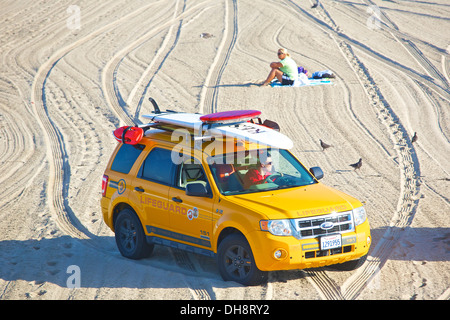 Bagnino di salvataggio nel suo SUV passato alla guida di una donna seduta da sola sulla spiaggia. Foto Stock