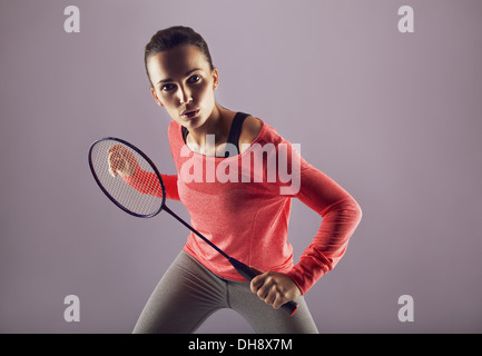 Bella ragazza tenendo badminton racchetta giocando contro uno sfondo grigio. Femmina persona sport badminton player guardando la fotocamera Foto Stock