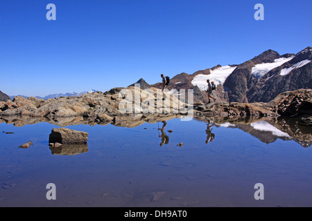 Due escursionisti di montagna escursionismo con bastoncini e montagne riflessa nell'acqua del lago alpino, Stubai, Alpi, Austria Foto Stock