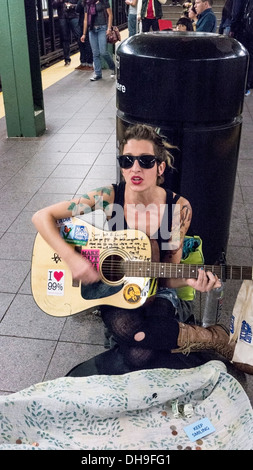 Piuttosto giovane donna con belle foglie tatuaggi sulle sue braccia e le unghie blu suona la chitarra e canta su Union Square piattaforma della metropolitana Foto Stock