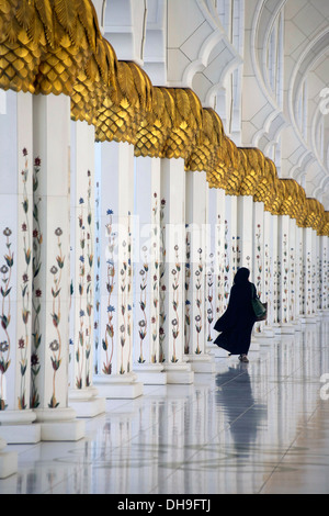 Lone donna cammina attraverso i pilastri della Sheikh Zayed Grande moschea Foto Stock