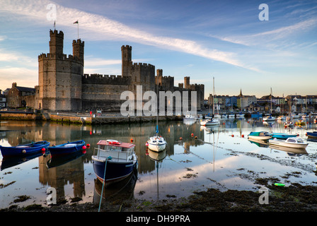 Bel tramonto su Caernarfon Castle in Galles con barche nel porto di bassa marea. Foto Stock